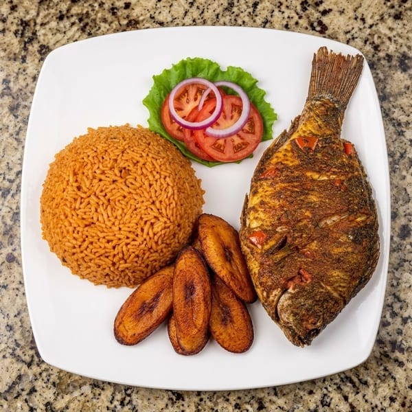 Fried fish, jollof rice, plantains, and fresh salad on a white plate.